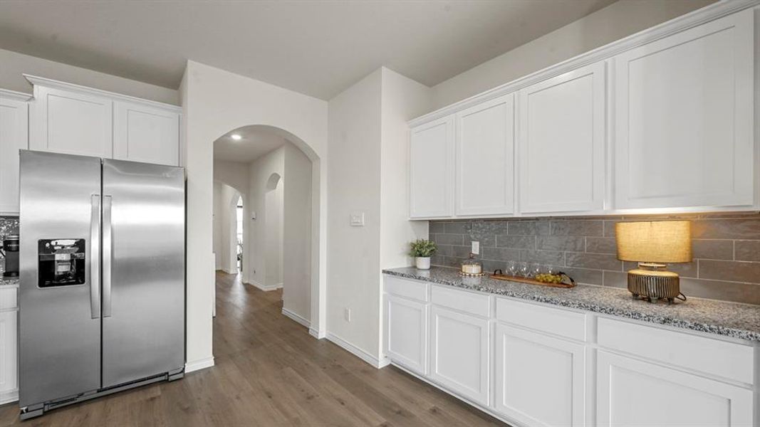 Kitchen featuring stainless steel refrigerator with ice dispenser, white cabinets, arched walkways, light stone counters, and backsplash
