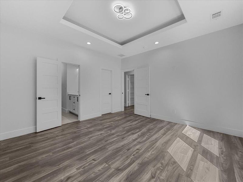 Unfurnished bedroom featuring a raised ceiling, light wood-type flooring, ensuite bathroom, and recessed lighting Unfurnished bedroom featuring a raised ceiling, light wood-type flooring, ensuite bathroom, and recessed lighting