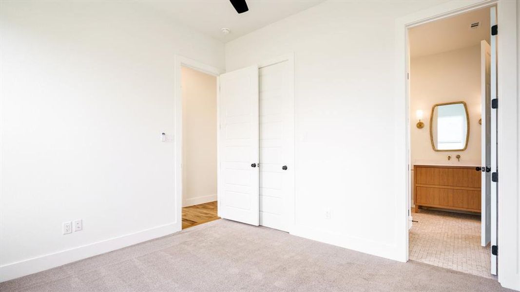 Unfurnished bedroom featuring ceiling fan, ensuite bath, light carpet, and a closet