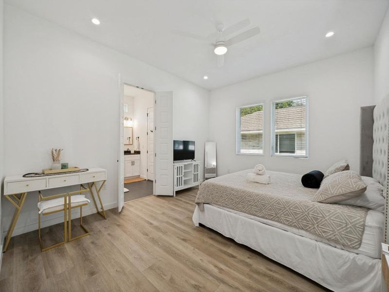 A naturally illuminated bedroom offers hardwood-style flooring, a ceiling fan, and convenient access to a private bathroom. A naturally illuminated bedroom offers hardwood-style flooring, a ceiling fan, and convenient access to a private bathroom.