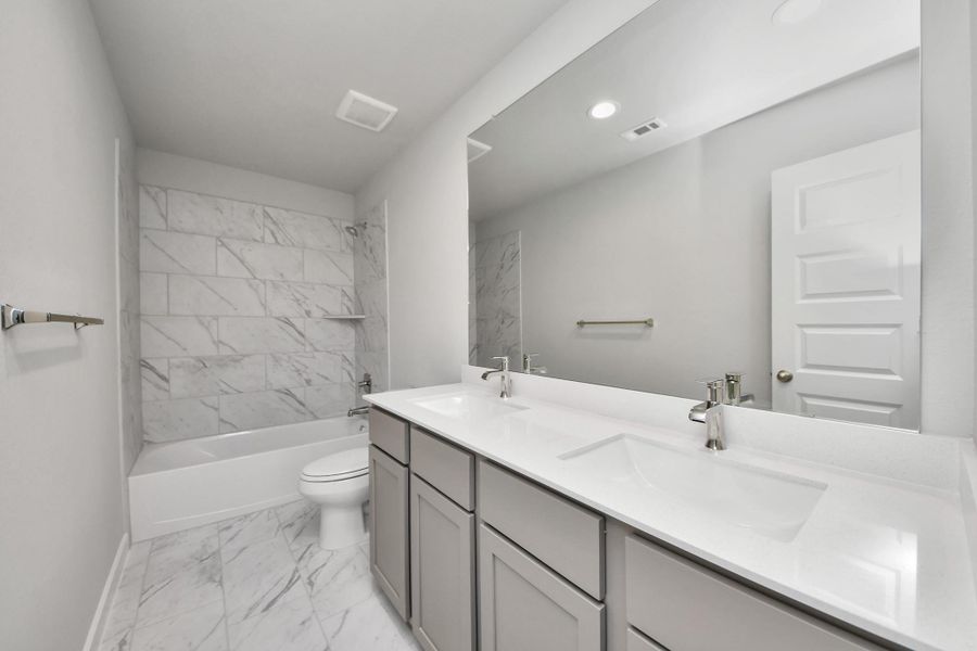 Secondary bath features tile flooring, bath/shower combo with tile surround, light stained wood cabinets, beautiful light countertop.