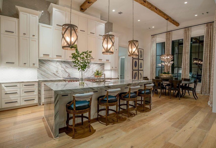 Luxury chef’s kitchen featuring marble waterfall island, custom cabinetry, designer pendant lighting, and open dining area.*Images depict previously completed homes by Roberson Building Group and are intended solely to showcase builder quality and craftsmanship.