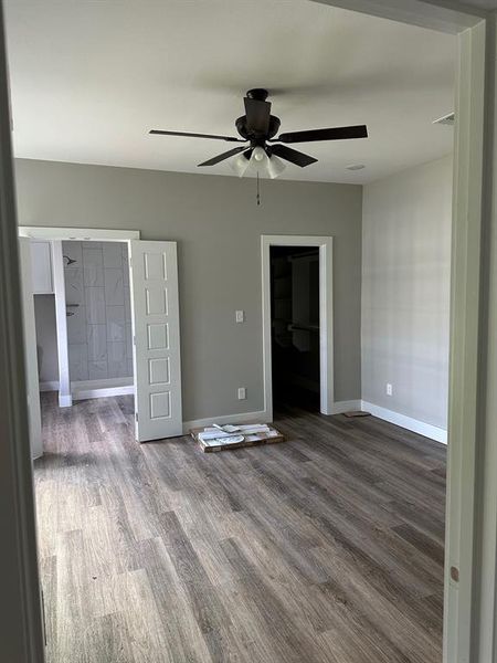 Unfurnished bedroom with wood finished floors, a walk in closet, a ceiling fan, and ensuite bath Unfurnished bedroom with wood finished floors, a walk in closet, a ceiling fan, and ensuite bath