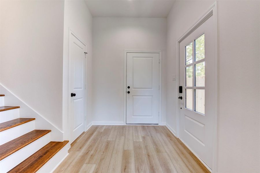Alternate view of the foyer with Alternate view of the foyer showcasing black hardware against a clean, neutral palette. To the left, a well-placed half bath offers convenience for guests while remaining tucked out of sight. Straight ahead, access to the spacious two-car garage enhances everyday functionality. hardware and neutral tones. To the left, a half bath is accessible to all residents and guests while remaining outside of view. Up ahead, access to a spacious two car garage