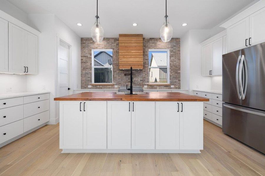 Kitchen featuring white cabinets, freestanding refrigerator, pendant lighting, and light wood finished floors