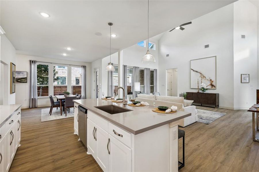 Open-concept living space featuring a central island with a built-in sink and seating, wood-finish flooring, recessed lighting, and a dining area with expansive windows
