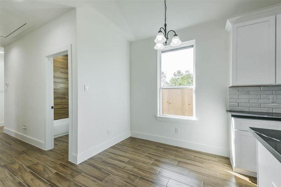 This is a bright, modern kitchen corner with sleek white cabinetry, a stylish backsplash, and wood-look flooring. It features a pendant light fixture and a window letting in natural light.