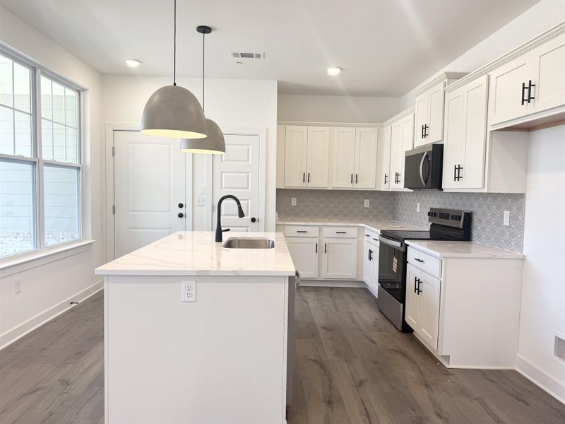 Kitchen featuring stainless steel appliances, a center island with sink, light stone counters, and dark wood-style floors
