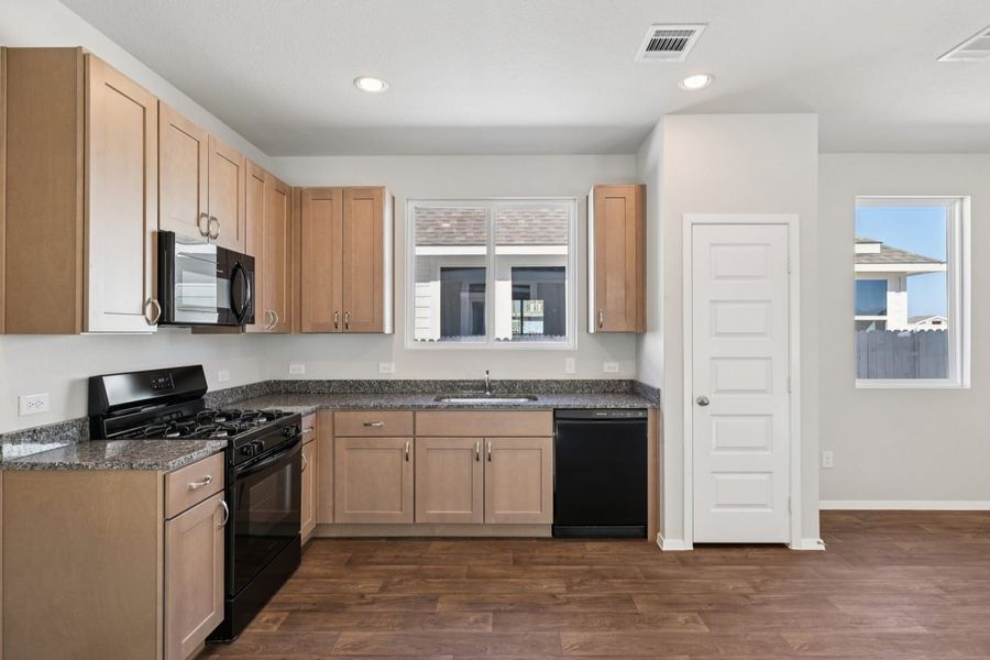 Image of a L-shaped kitchen with brown cabinets, granite countertops, black appliances and a window above the sink