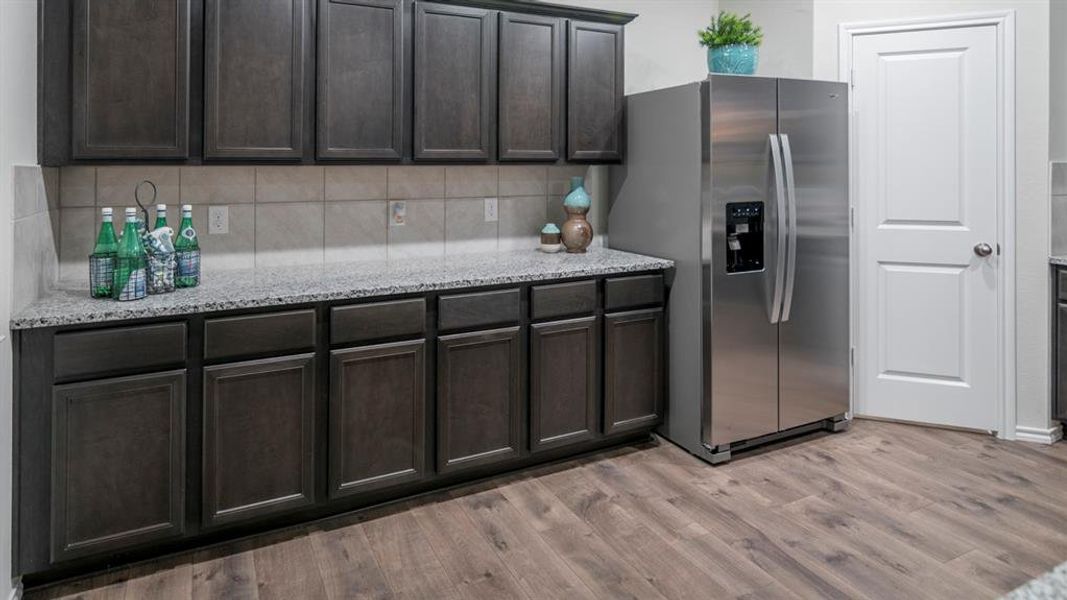 Kitchen with light stone countertops, stainless steel fridge with ice dispenser, light wood finished floors, backsplash, and dark wood finish cabinets