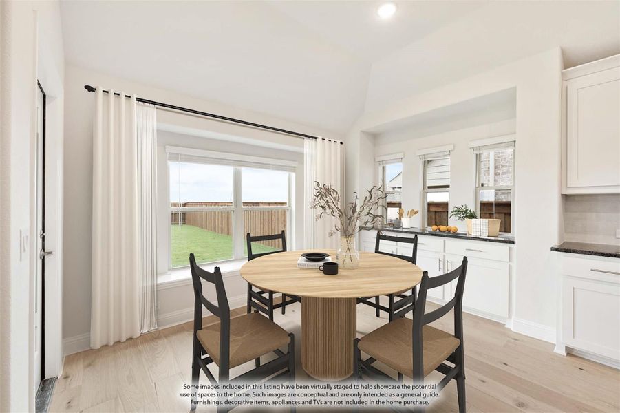 Dining area with round wood table, four chairs, large windows, and light hardwood floors adjacent to white kitchen