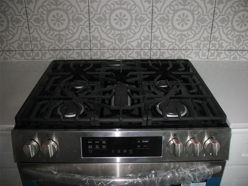 Kitchen view of pot filler, stainless steel range with gas cooktop, and light stone counters