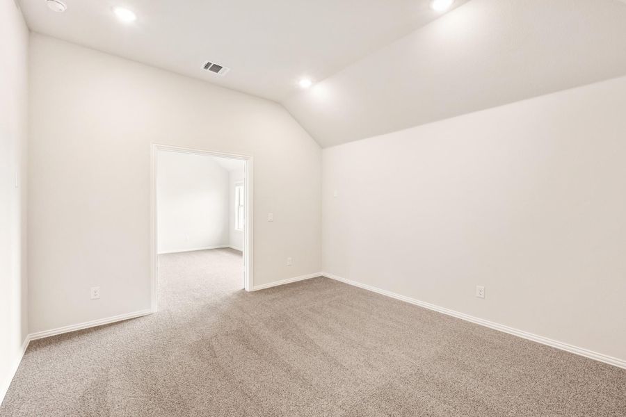 Empty bedroom with vaulted ceiling, gray carpet, and white walls with doorway to adjoining room Empty bedroom with vaulted ceiling, gray carpet, and white walls with doorway to adjoining room