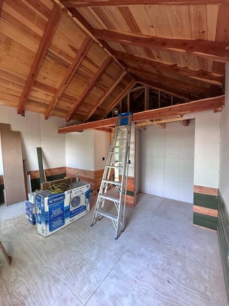 Exposed wooden beams and high vaulted ceilings create a spacious and inviting atmosphere in this room under construction.