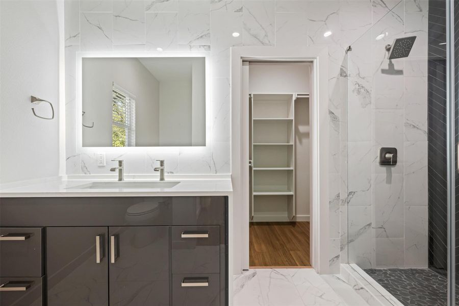 Bathroom with light marble finish floors, a marble finish shower, vanity, and a walk in closet