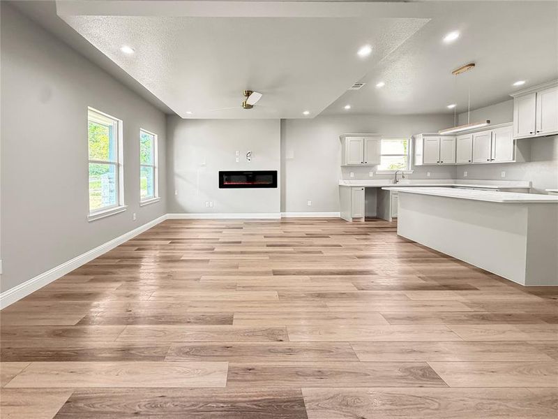 Open-concept living space featuring wood-finish flooring, an electric fireplace, recessed lighting, white cabinetry, and white countertops