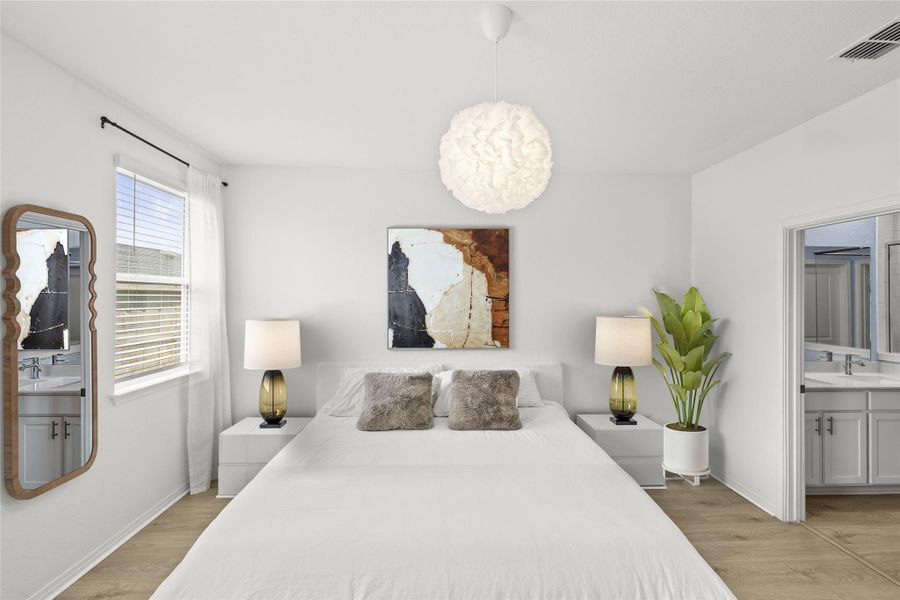 Relaxation awaits in this bedroom featuring durable wood-look flooring and a connecting private bathroom.