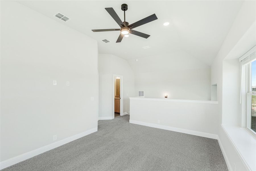 Empty bedroom with vaulted ceiling, ceiling fan, gray carpet, and door to ensuite bathroom