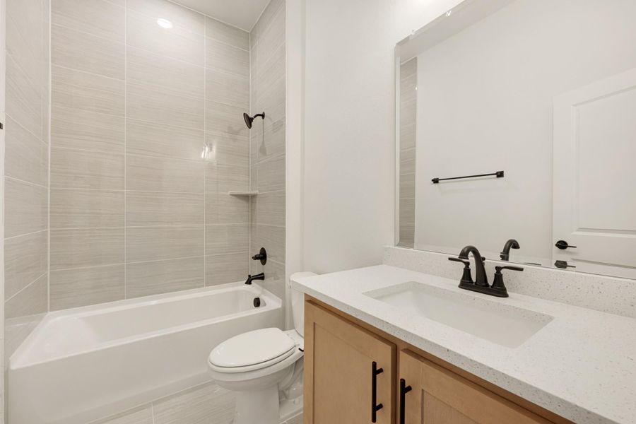 Bathroom with tiled tub-shower combo, wood vanity with quartz countertop, and matte black fixtures