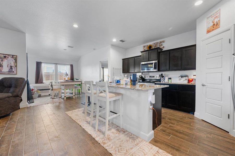 Kitchen featuring open floor plan, light stone countertops, a kitchen island with sink, a breakfast bar area, and stainless steel appliances Kitchen featuring open floor plan, light stone countertops, a kitchen island with sink, a breakfast bar area, and stainless steel appliances