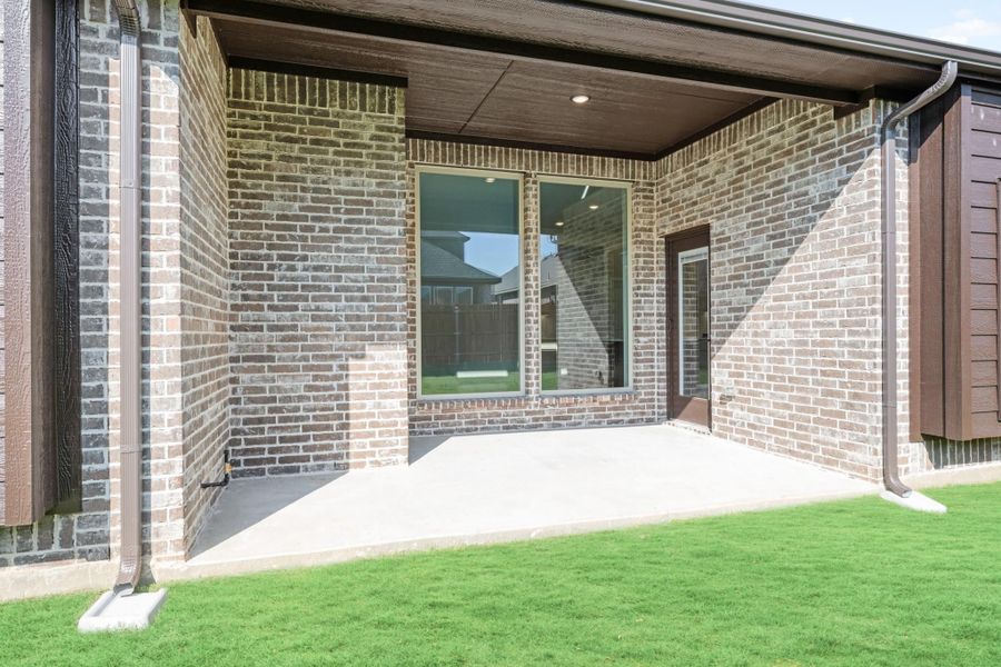 Covered back patio with brick exterior, concrete floor, large sliding glass door, and green lawn