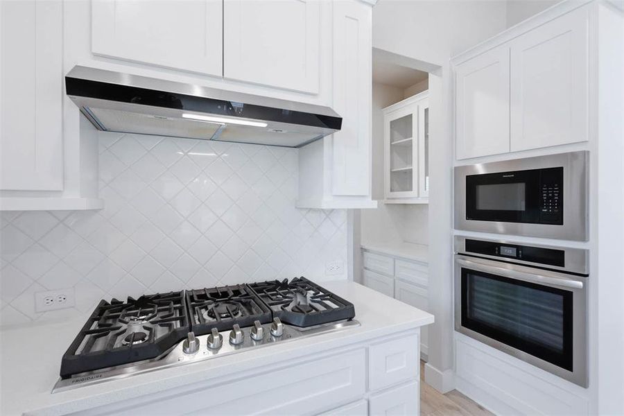 Kitchen detail featuring gas cooktop, built-in oven, and sleek modern finishes. Looking into butlers pantry