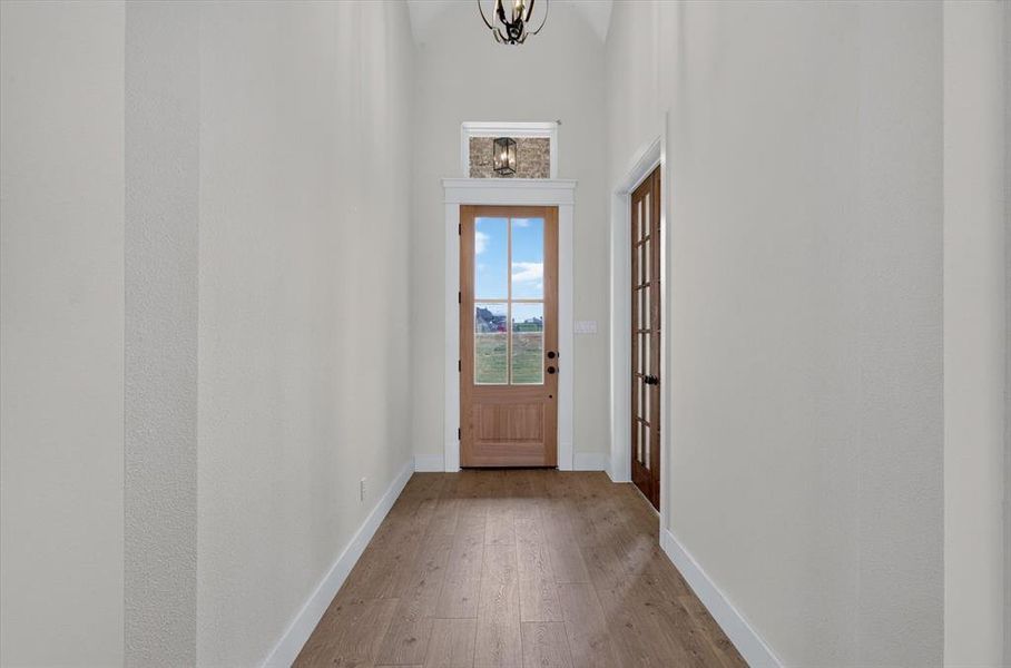 Entryway featuring vaulted ceilings, wood-finish flooring, and a natural wood front door with glass panels Entryway featuring vaulted ceilings, wood-finish flooring, and a natural wood front door with glass panels