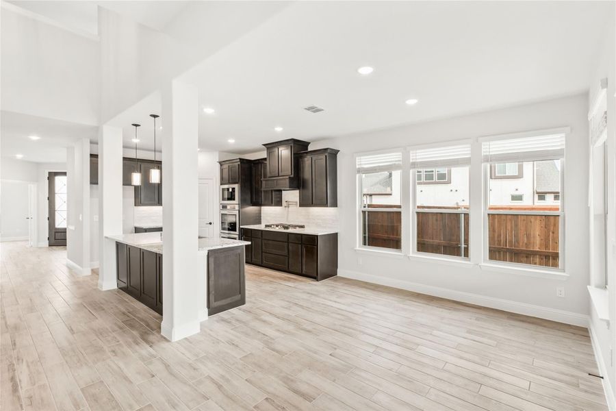 Open-concept kitchen with dark cabinets, center island, and light wood floors flowing into living area Open-concept kitchen with dark cabinets, center island, and light wood floors flowing into living area