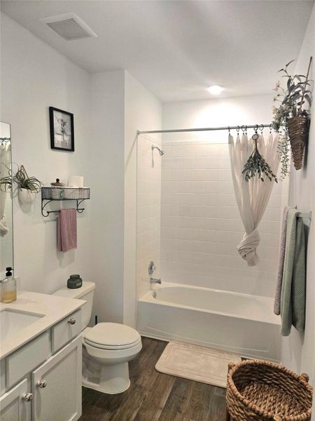 Bathroom featuring a full-size bathtub with subway tile surround, wood-finish flooring, a contemporary vanity with a single sink, and a toilet