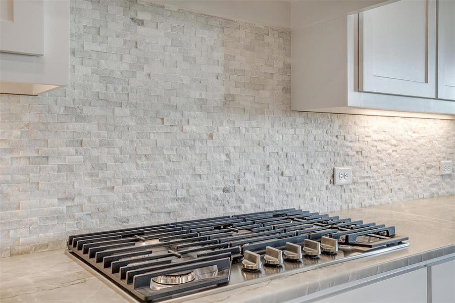 Details with backsplash, light stone counters, and stainless steel gas stovetop