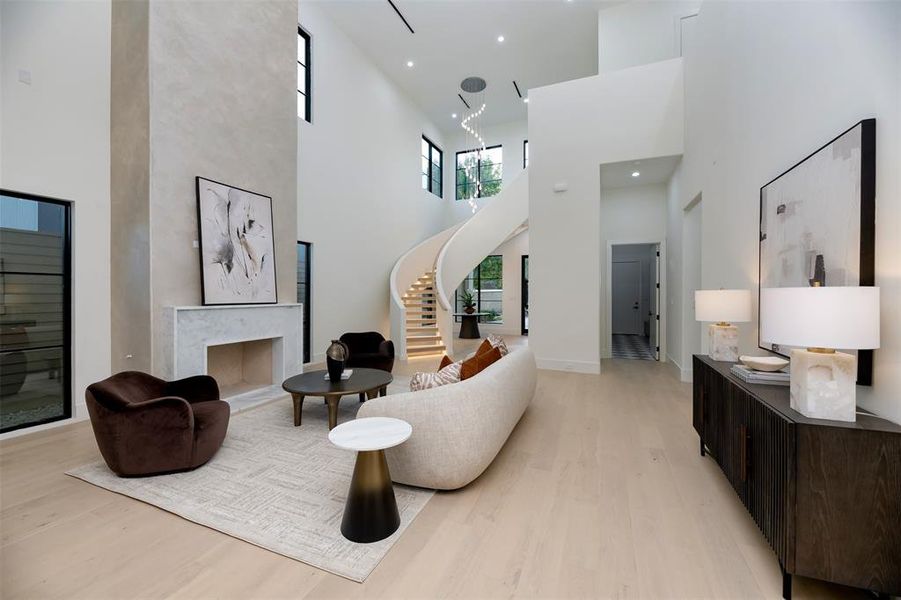 Living area with light wood-style flooring, stairway, a high end fireplace, a towering ceiling, and recessed lighting
