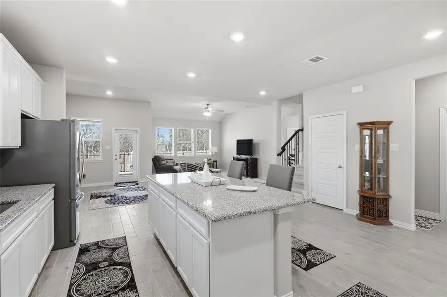 Open-concept kitchen featuring an oversized island with granite countertops, white cabinetry, and stainless steel appliances
