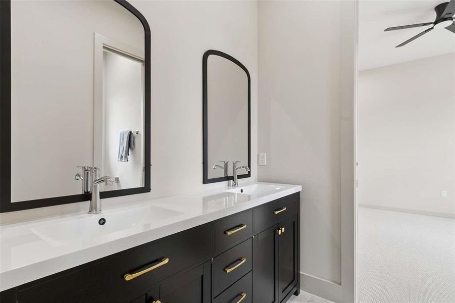 Dual sink vanity featuring dark wood cabinetry with gold-tone hardware, white countertops, and contemporary black-framed arched mirrors. Dual sink vanity featuring dark wood cabinetry with gold-tone hardware, white countertops, and contemporary black-framed arched mirrors.