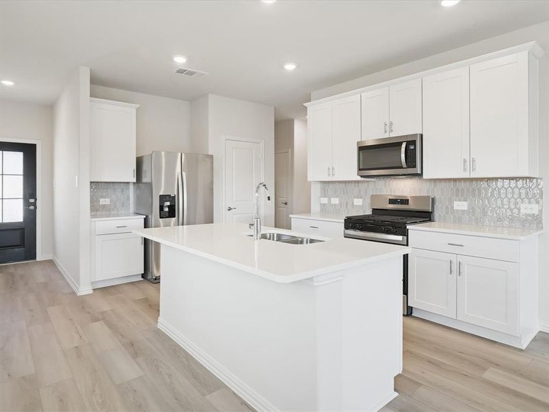 Kitchen with stainless steel appliances, decorative backsplash, a kitchen island with sink, white cabinetry, and light wood-style floors