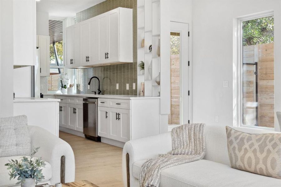 Kitchen with decorative backsplash, white cabinets, light wood-style floors, light stone counters, and dishwasher