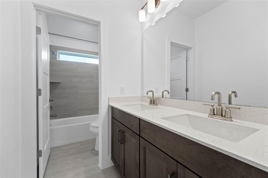 This well-appointed secondary bathroom offers exceptional functionality with its rich, dark wood double vanity topped with pristine white countertops and convenient dual undermount sinks. Sleek, polished chrome fixtures complement the expansive vanity mirror and chic light vanity fixture.