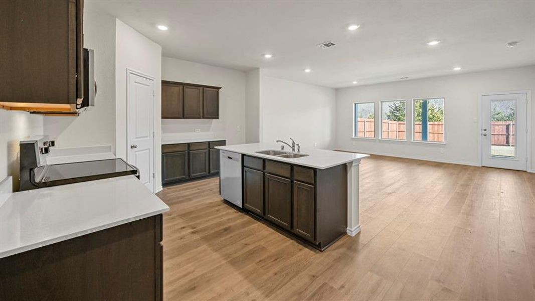 Open-concept kitchen featuring an island with an integrated sink, dark wood-finish cabinetry, and light-colored countertops