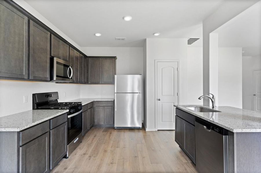 Kitchen with sink, light wood-type flooring, light stone counters, and stainless steel appliances