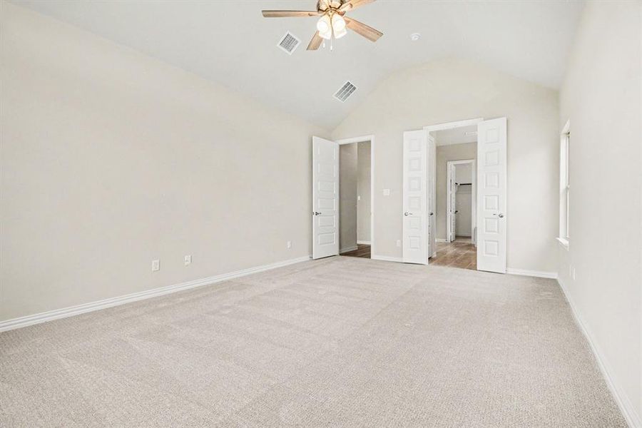 Vaulted ceiling bedroom featuring plush light-toned carpeting, neutral wall finishes, a ceiling fan with integrated lighting, and multiple panel doors Vaulted ceiling bedroom featuring plush light-toned carpeting, neutral wall finishes, a ceiling fan with integrated lighting, and multiple panel doors