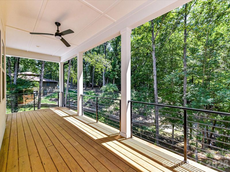Lakefront covered deck with modern cable railing and ceiling fan, offering peaceful wooded views and the perfect setting to relax and enjoy waterfront living.