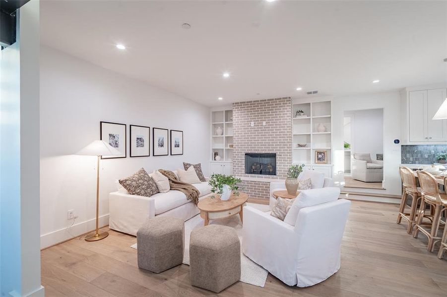 Living room with light hardwood flooring, brick gas fireplace, and built in features