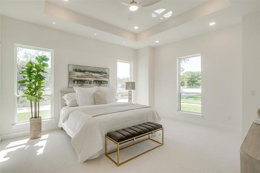 Bedroom with multiple windows, a tray ceiling, ceiling fan, and light colored carpet