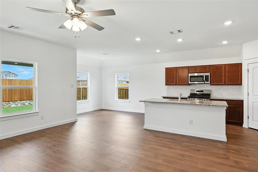 Kitchen featuring stainless steel appliances, decorative backsplash, a ceiling fan, dark wood-style floors, and light stone counters Kitchen featuring stainless steel appliances, decorative backsplash, a ceiling fan, dark wood-style floors, and light stone counters