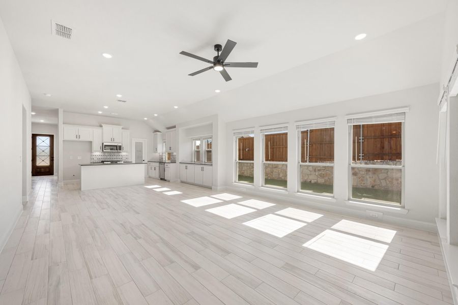 Open living area with light wood floors, ceiling fan, and open-concept kitchen with white cabinets in background