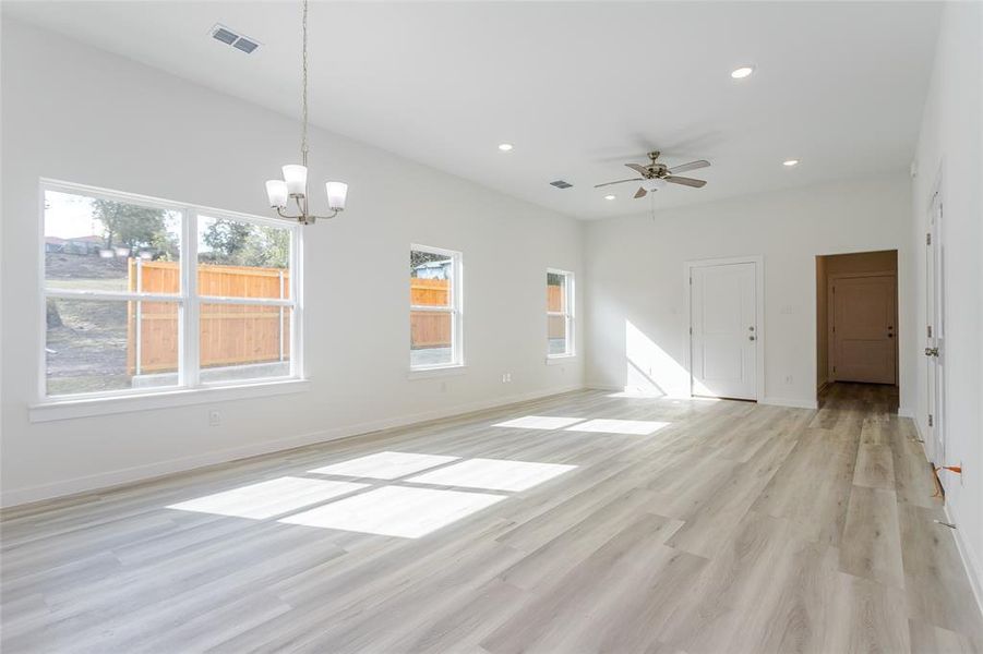 Unfurnished living room featuring ceiling fan with notable chandelier and light hardwood / wood-style flooring