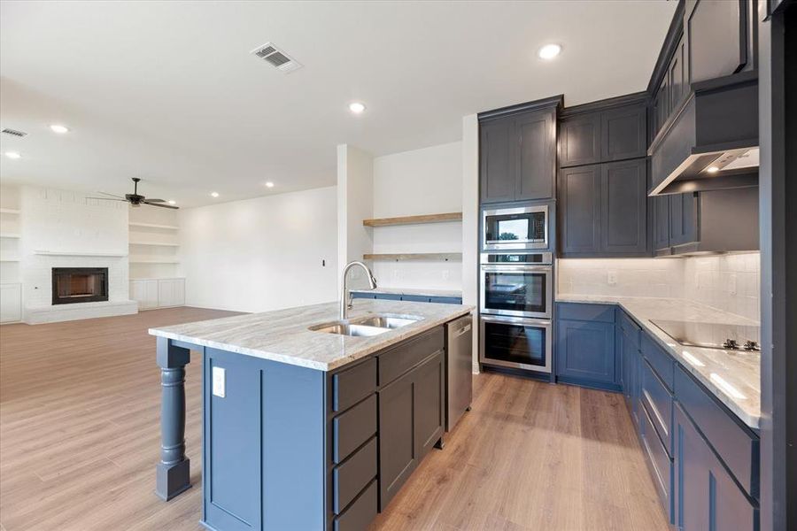 Kitchen featuring light hardwood / wood-style flooring, a center island with sink, a brick fireplace, and sink