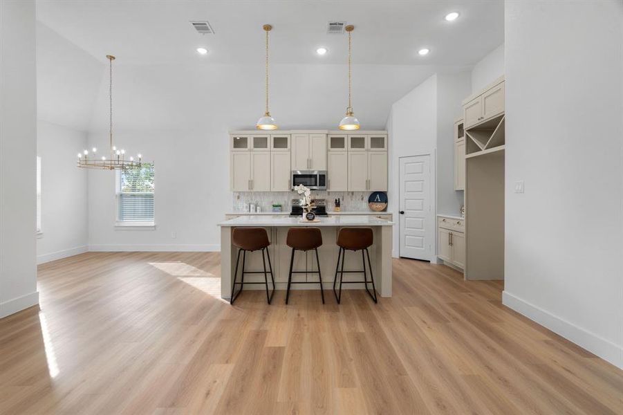 Kitchen featuring a breakfast bar, decorative light fixtures, a center island with sink, glass insert cabinets, and recessed lighting