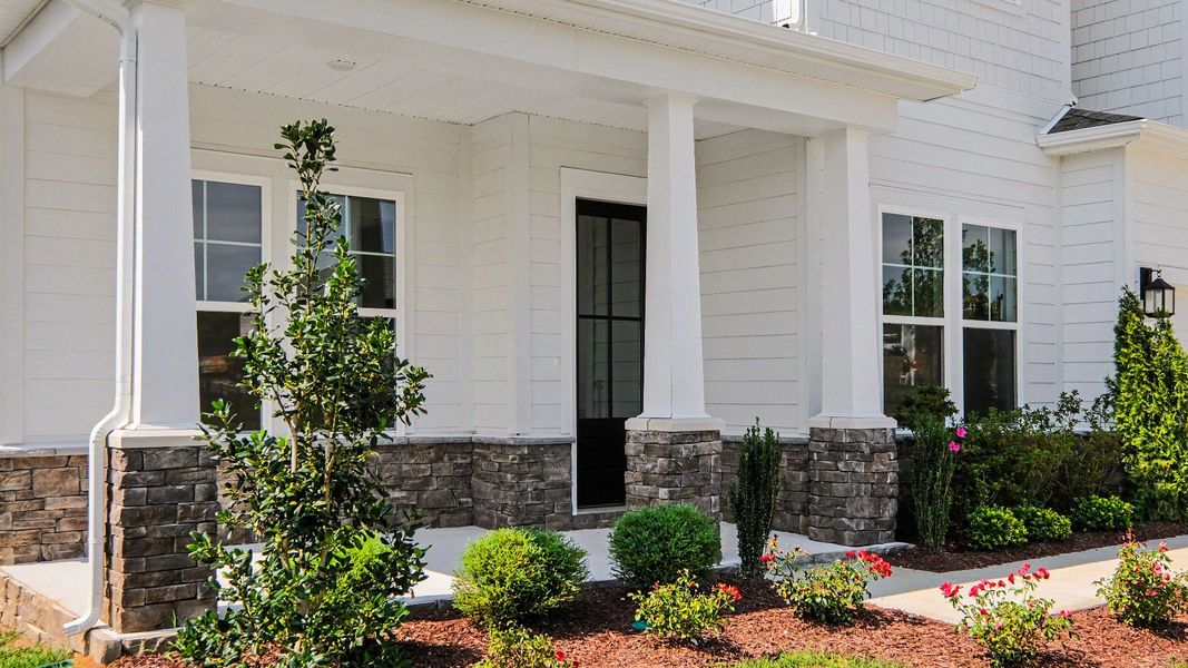 Covered front porch and entry door to home with landscaping