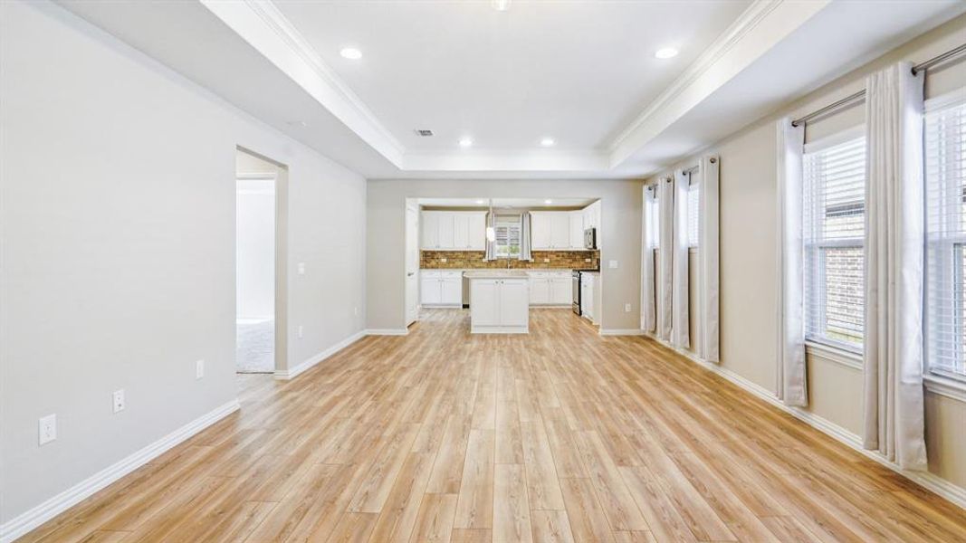 Unfurnished living room featuring light wood-type flooring, crown molding, recessed lighting, and a raised ceiling Unfurnished living room featuring light wood-type flooring, crown molding, recessed lighting, and a raised ceiling