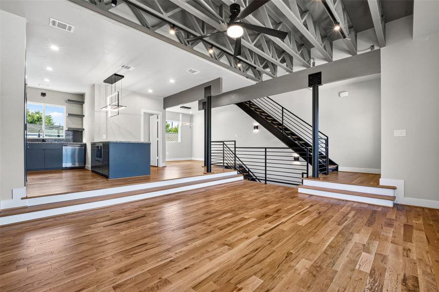 The open-plan second floor is the dramatic heart of the home. Soaring exposed trusses tie the living, kitchen, and dining areas together. Wood floors, recessed living room, and modern light fixtures run throughout.